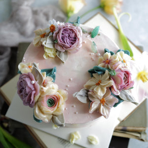 
                  
                    Load image into Gallery viewer, A light pink buttercream cake with white, pink and purple assorted buttercream flowers on top. The cake also has edible sugar pearls delicately scattered on top and around it.
                  
                