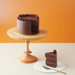 A chocolate cake with a slice cut out from it to show the cross section. The chocolate cake looks rich and moist, and it is coated in chocolate ganache.