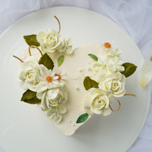 
                  
                    Load image into Gallery viewer, A heart shaped cake with white buttercream base, and ivory buttercream flowers on top of the cake.
                  
                