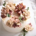 Ivory buttercream base with various shade of pink buttercream flowers on top in a crescent shape.