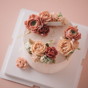 
                  
                    Load image into Gallery viewer, Light pink buttercream cake with red, pink and blush buttercream flowers on top in a wreath style. There are edible sugar pearls scattered on top.
                  
                