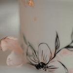 A close up of the cake, that focuses on a light pink edible wafer flower, and hand painted black outline of a flower.