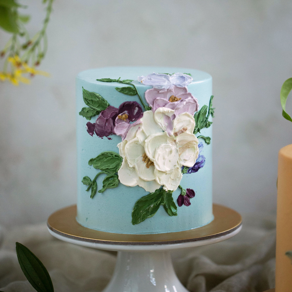 
                  
                    Load image into Gallery viewer, A light blue buttercream cake with white and purple palette knife buttercream flowers.
                  
                