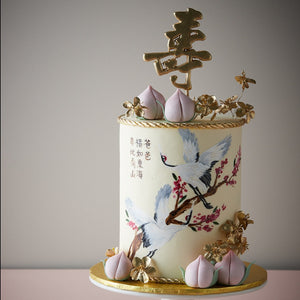 
                  
                    Load image into Gallery viewer, Ivory fondant base with hand painted cranes, and little fondant peaches. Mandarin words are hand painted on the front of the cake. Edible golden flowers adorn the cake.
                  
                