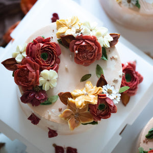 
                  
                    Load image into Gallery viewer, Blush coloured buttercream cake with dark red, orange and white buttercream flowers in assorted shapes on top.
                  
                