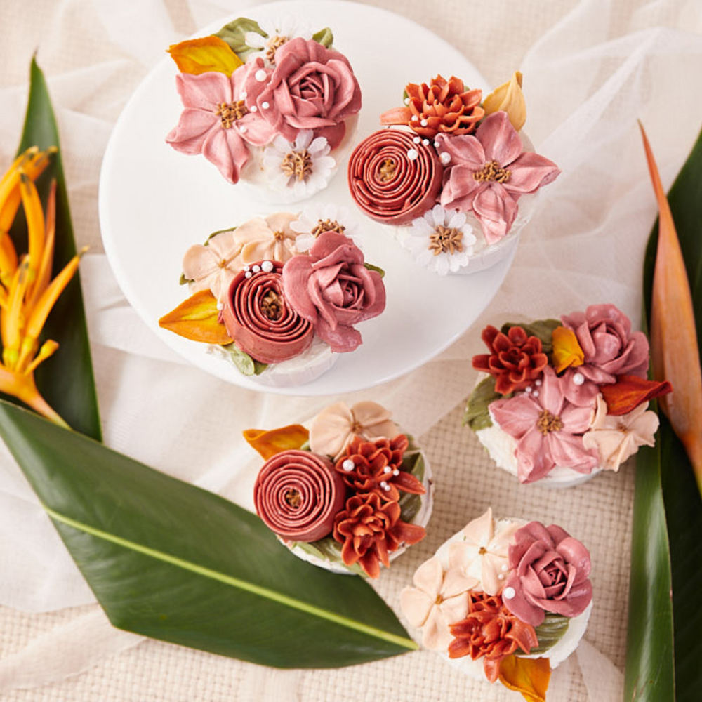 There are six cupcakes in the image, with three of them being in the center focus. The cupacakes are decorated with hand piped buttercream flowers in different styles, and they are all different shades of pink.