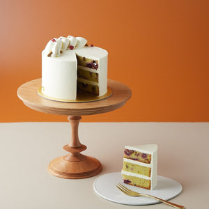 
                  
                    Load image into Gallery viewer, A rose pistachio cake with a slice cut out to show the cross section. The cake  has a white buttercream coating, and the slice shows a neat moist looking cake. The cake itself is pistachio green, and it has bits of pink raspberries inside. The top of the cake has dried rose petals sprinkled lightly.
                  
                
