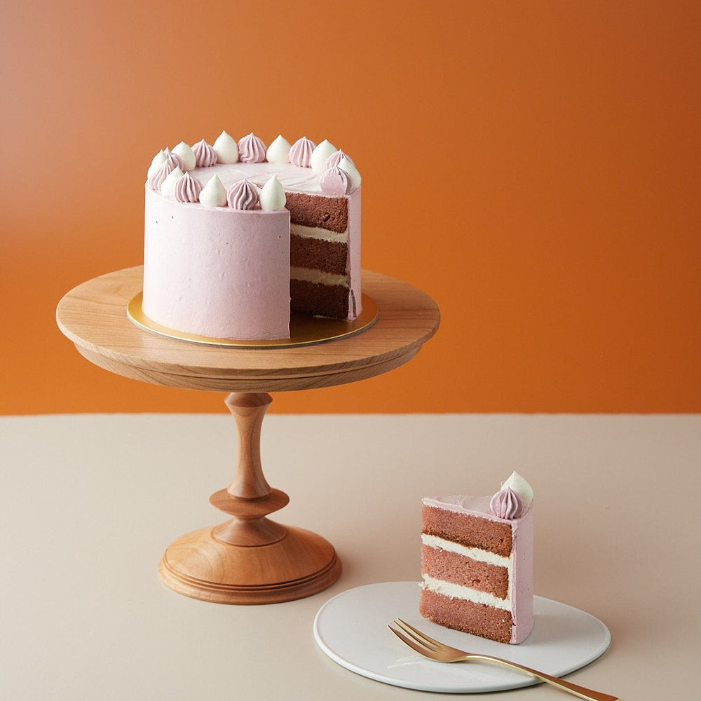 A strawberry yogurt cake with a slice cut to show the cross section. The cake has a pink buttercream coating, and the inner cake is a darker shade of pink. The cake looks moist and has a tight crumb.