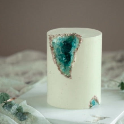 A tall but slim white fondant cake. It has a chunk removed and replaced with edible turquoise rock candy, to resemble turquoise crystals. This cake looks like a geode has been cut open.