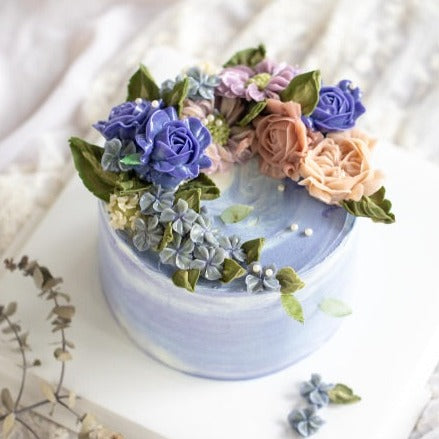 A bluish purple marbled with white buttercream cake with purple, coral and pink buttercream flowers on top.