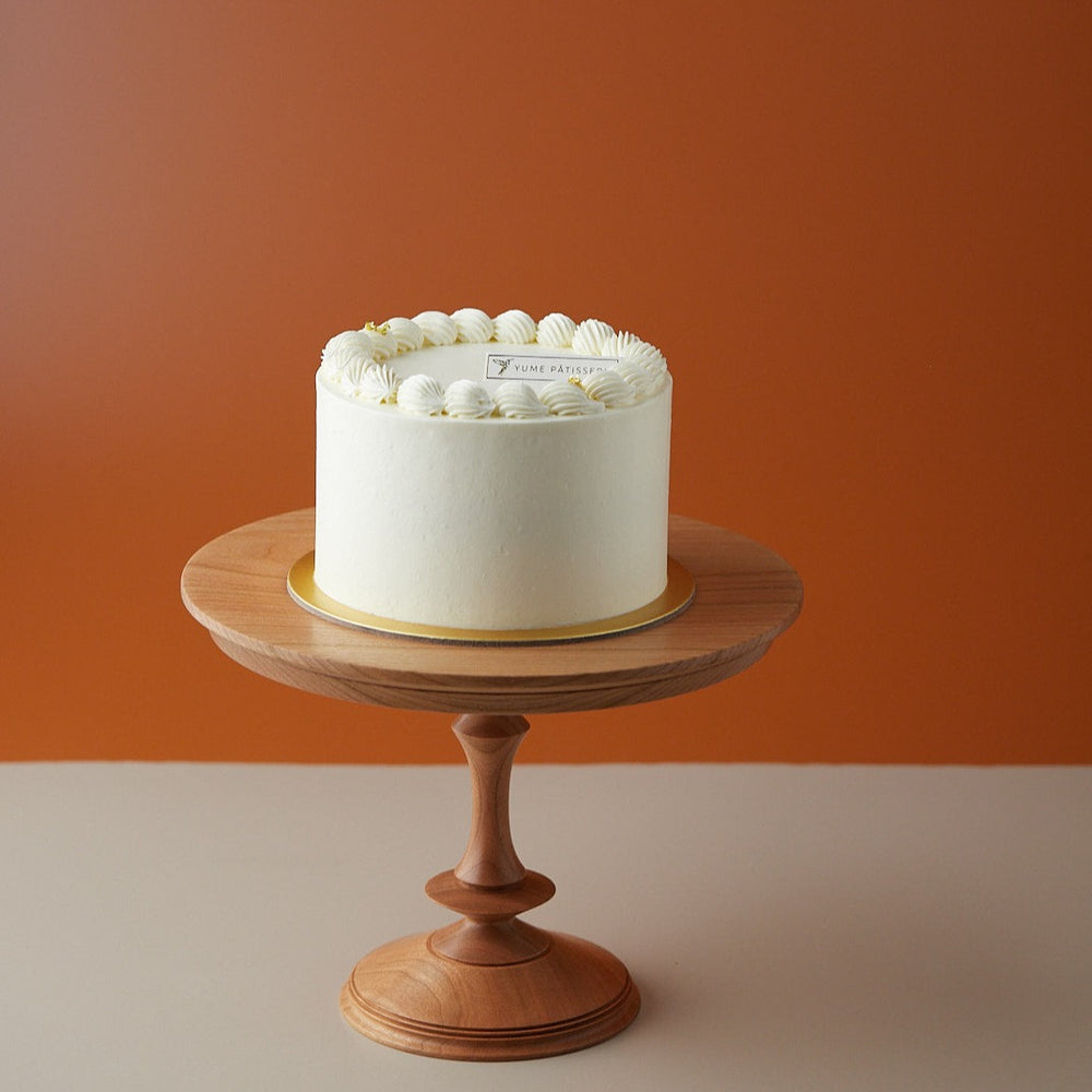 A white buttercream cake with sprinkles of elderflower petals on top. The cake is elegant and simplistic.