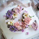A light purple buttercream cake with pink, purple and white buttercream flowers.