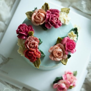 A light blue buttercream cake with light pink, dark pink and red buttercream roses on top. The cake also has accents of white.