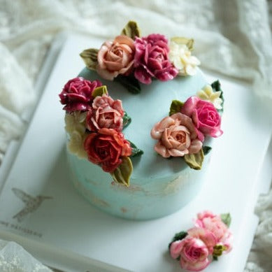 A light blue buttercream cake with light pink, dark pink and red buttercream roses on top. The cake also has accents of white.