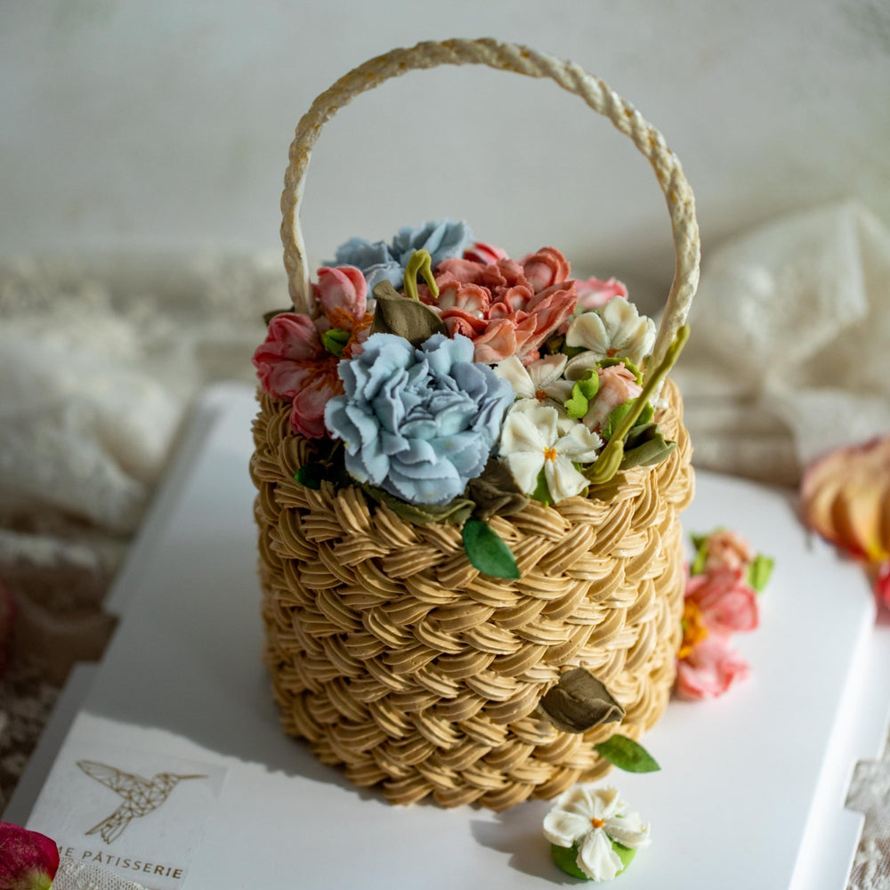 Realistic flower basket cake. This cake has been carved and decorated to look like a real flower basket, with light brown buttercream that resembles a woven basket. The cake has assorted buttercream flowers in blue, pink and white spilling out of the top, and looks incredibly realistic