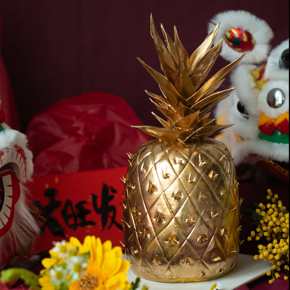 A golden cake that has been carved into the shape of a pineapple, with gold fondant pineapple stem. The cake is very realistic.