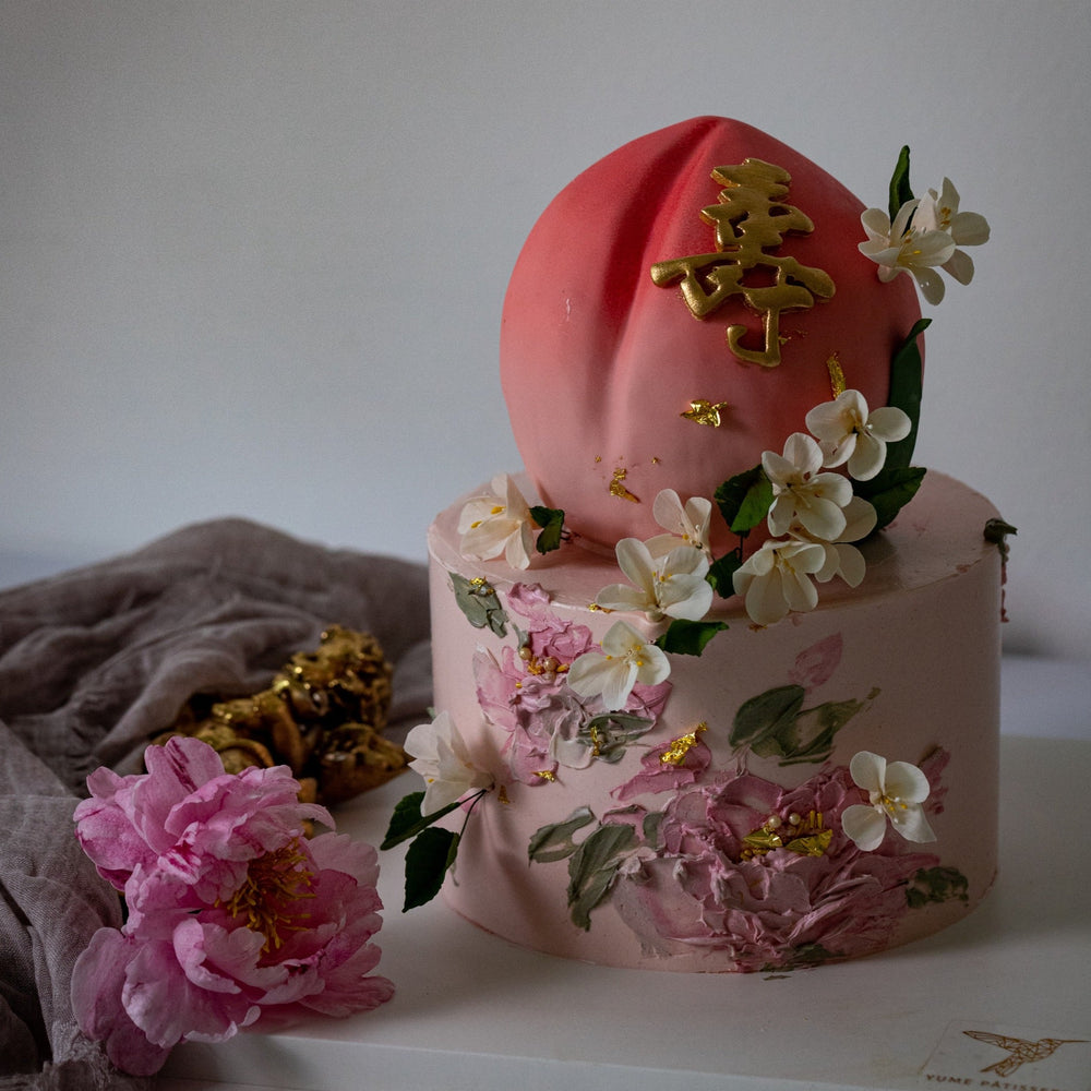 Two tier cake with the top tier carved into the shape of a peach, and the bottom tier a sweet shade of pink. The cake has hand painted buttercream flowers, and white edible wafer flowers.
