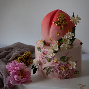 
                  
                    Load image into Gallery viewer, Two tier cake with the top tier carved into the shape of a peach, and the bottom tier a sweet shade of pink. The cake has hand painted buttercream flowers, and white edible wafer flowers.
                  
                