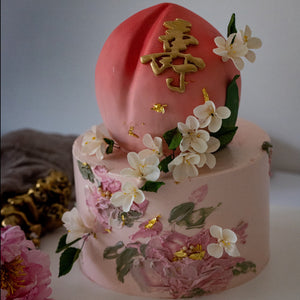 
                  
                    Load image into Gallery viewer, Two tier cake with the top tier carved into the shape of a peach, and the bottom tier a sweet shade of pink. The cake has hand painted buttercream flowers, and white edible wafer flowers.
                  
                