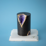 A tall and slim cake, this cake is covered in a dark bluish purple fondant. The fondant has speckles of gold splattered on it that resemble stars. A chunk of the cake has been cut out adn replaced with edible purple rock candy that resemble Amethyst gems, so the cake looks like a geode.