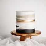 A cake with a marbled white and beige fondant base that resembles sand. The bottom of the cake has black fondant that resembles a stone floor, and the middle of the cake has a golden faultline.