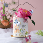 A small but tall cake with a white fondant base, and watercolour style flowers on an edible icing sheet wrapped around the cake. There are edible wafer butterflies on the cake, along with a realistic edible wafer peopny on top. The peony is a deep shade of pink, and looks very detailed. There are edible sugar pearls scattered around the cake.