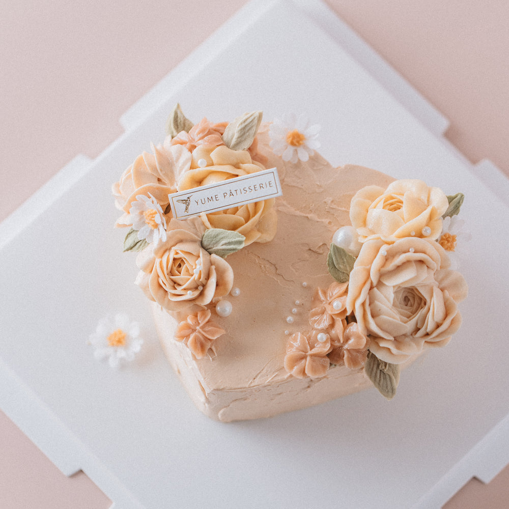 
                  
                    Load image into Gallery viewer, A light peachy pink heart shaped cake with light pink buttercream flowers and sugar pearls.
                  
                