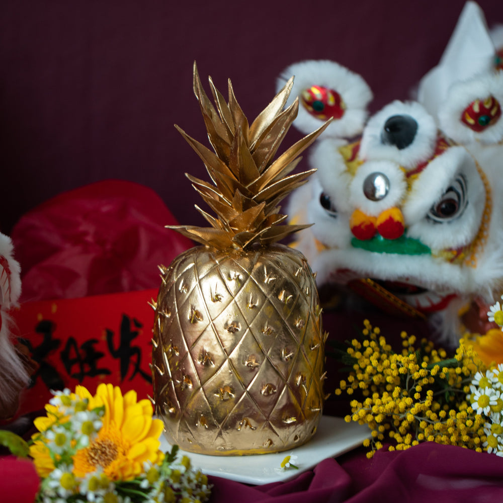 A golden cake that has been carved into the shape of a pineapple, with gold fondant pineapple stem. The cake is very realistic.