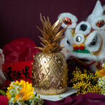 A golden cake that has been carved into the shape of a pineapple, with gold fondant pineapple stem. The cake is very realistic.