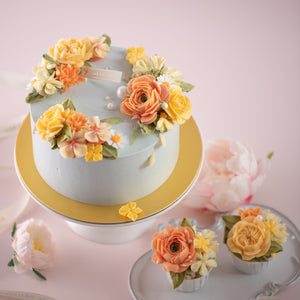 
                  
                    Load image into Gallery viewer, A pale blue cake with bright coral and yellow hand piped buttercream flowers. The cake also has some sugar pearls delicately scattered on top. The flowers look incredibly lifelike. Next to the cake, there are some matching cupcakes with the same yellow and coral buttercream flowers.
                  
                