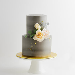 
                  
                    Load image into Gallery viewer, A two tier wedding cake with a concrete grey buttercream base. The buttercream has streaks of lighter grey marbled into it. There are some light pink and ivory edible sugar roses in the middle, along with some pale edible green sugar leaves. The flowers look incredibly realistic.
                  
                