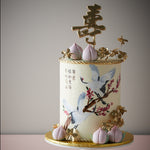 Ivory fondant base with hand painted cranes, and little fondant peaches. Mandarin words are hand painted on the front of the cake. Edible golden flowers adorn the cake.