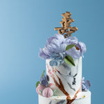 A close up on the top tier of the cake, with the hand painted cranes and the large sugar peonies. The peonies are lilac in colour, and the sugar hydrangeas are a shade of pale blue. 