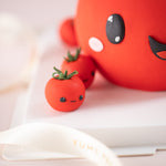 A close up of one of the fondant cherry tomatoes on the cake board. It has a mischievous cat-like expression, going :3