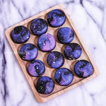 Round macarons that resemble the galaxy. The macarons are swirled purple, pink and black, and they have speckles of silver that resemble stars in the milkyway.