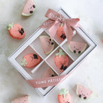 A white box with a transparent window. Inside the box there are assorted macarons that look like jellycat watermelon and strawberry plushies. The macarons are super cute.