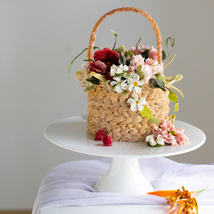 
                  
                    Load image into Gallery viewer, A cake that has been decorated to look like a flower basket. The outside has light brown buttercream that has been piped to resemble a woven basket, and it has assorted buttercream flowers in red, pink and white spilling out of it. It is a realistic flower basket cake.
                  
                